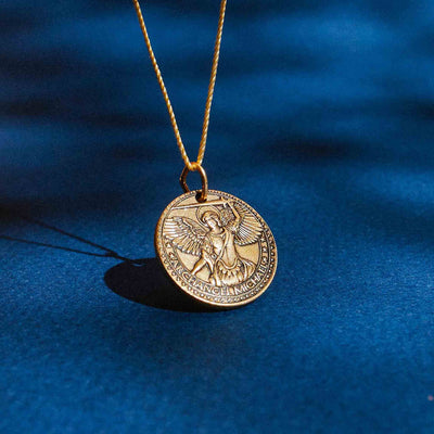 a gold necklace with a round medallion pendant. The medallion has a picture of a winged angel on it. The text “ARCHANGEL MICHAEL” is engraved around the edge of the medallion.