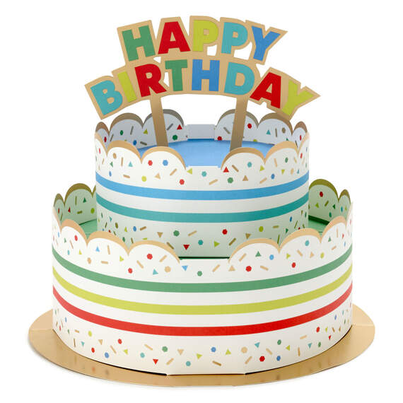 Hallmark 3D pop-up birthday cake paper decor with rainbow stripes, sprinkles, gold foil accents, and "Happy Birthday" banner.

