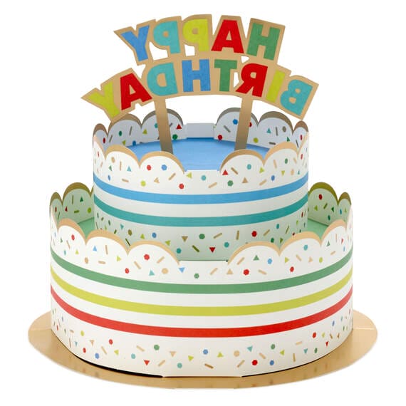 Hallmark 3D pop-up birthday cake paper decor with rainbow stripes, sprinkles, gold foil accents, and "Happy Birthday" banner.

