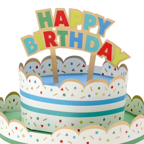 Hallmark 3D pop-up birthday cake paper decor with rainbow stripes, sprinkles, gold foil accents, and "Happy Birthday" banner.

