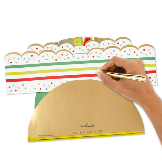 Hallmark 3D pop-up birthday cake paper decor with rainbow stripes, sprinkles, gold foil accents, and "Happy Birthday" banner.

