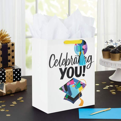 Hallmark large graduation gift bag with colorful mortarboard, black lettering on white, gift tag, and tassel attachment.

