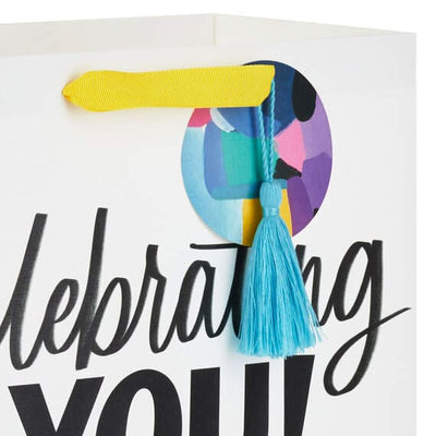 Hallmark large graduation gift bag with colorful mortarboard, black lettering on white, gift tag, and tassel attachment.

