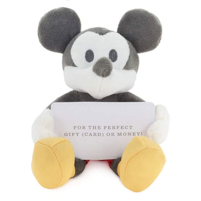 stuffed Mickey Mouse plush holding a gift card with a red background with white snowflakes. The text on the gift card reads ”FOR THE PERFECT GIFT (CARD) OR MONEY