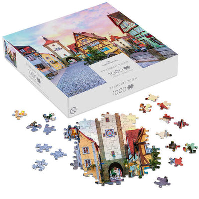 Hallmark 1000-piece puzzle featuring a European village with shops, archways, and a pink morning sky.

