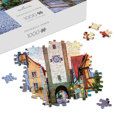 Hallmark 1000-piece puzzle featuring a European village with shops, archways, and a pink morning sky.

