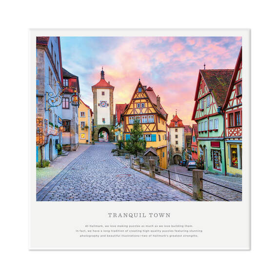 Hallmark 1000-piece puzzle featuring a European village with shops, archways, and a pink morning sky.

