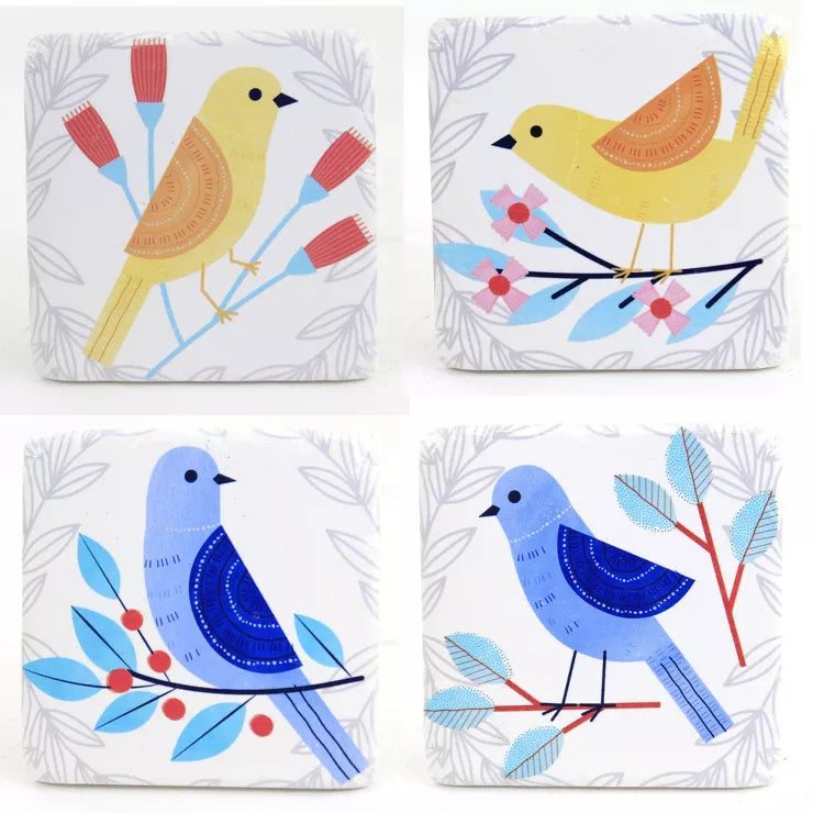 A set of four white resin coasters with blue and yellow birds perched on leafy branches in vibrant colors