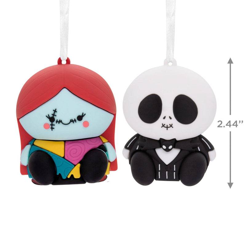 Two Nightmare Before Christmas ornaments featuring Jack Skellington and Sally. Jack is a skeleton with a pinstriped suit and bat bowtie. Sally has ragdoll stitching and a patchwork dress. They are connected by a red ribbon