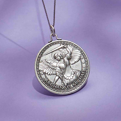 The pendant is siiver and shaped like a rounded shield. In the center of the pendant is a detailed image of a winged angel.The text "ARCHANGEL MICHAEL" is written around the edge of the pendant in a decorative font.