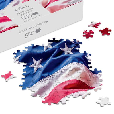 Hallmark 550-piece puzzle showing a close-up of the rippling American flag with red, white, and blue stars and stripes.


