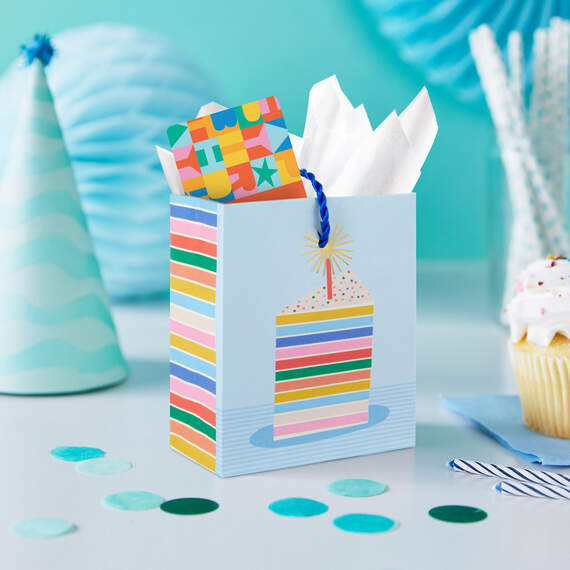 Mini gift bag with colorful layered cake slice design, gold foil accents, and pale blue background with twisted cord handles.

