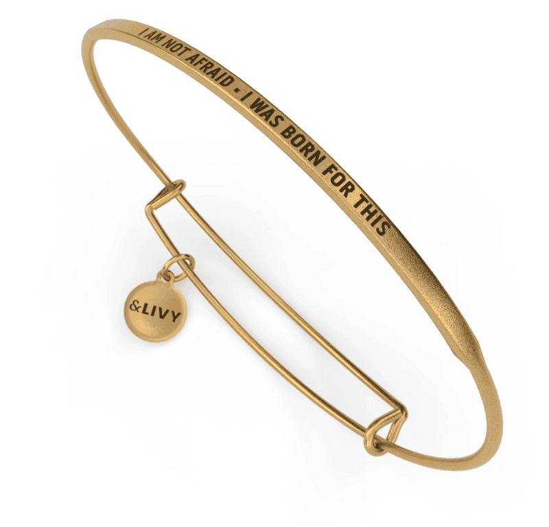 Gold bangle bracelet with the words "I am not afraid - I was born for this" engraved on it. The lettering is cursive.