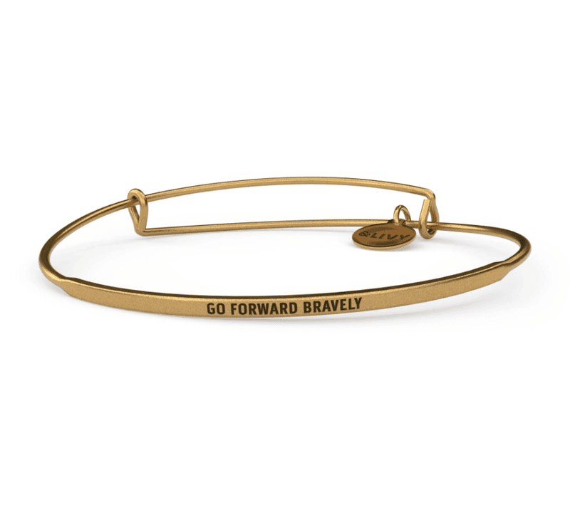 Gold bangle bracelet with the words "go forward bravely" engraved on it. 