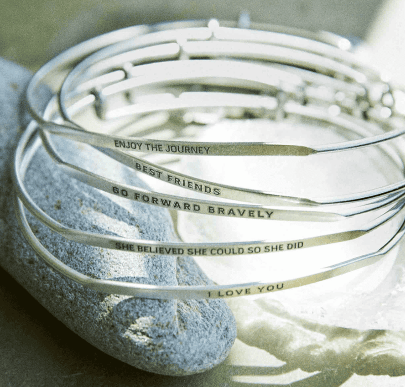 Stack of silver bangle bracelets with words engraved on them. Words include "she believed she could so she did". 