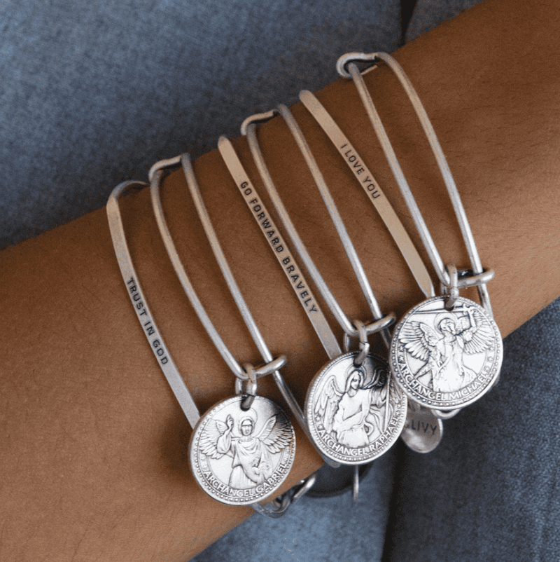 Stack of silver bangle bracelets with words engraved on them. Words include "Trust in God".