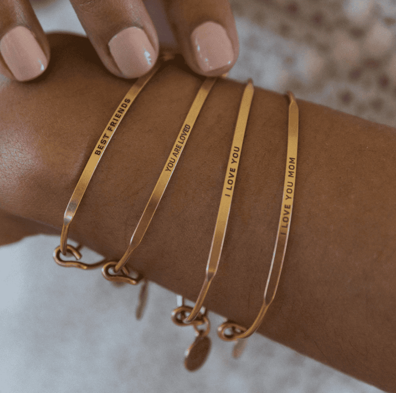 Gold bangle bracelet with the words "I love you mom" engraved on it.