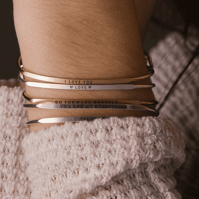 Stack of silver bangle bracelets with words engraved on them. Words include "LOVE".