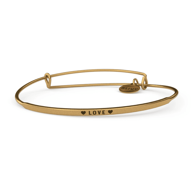 Gold bangle bracelet with a heart-shaped charm and the word "love" engraved on it.