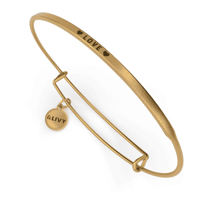 Gold bangle bracelet with a heart-shaped charm and the word "love" engraved on it. 