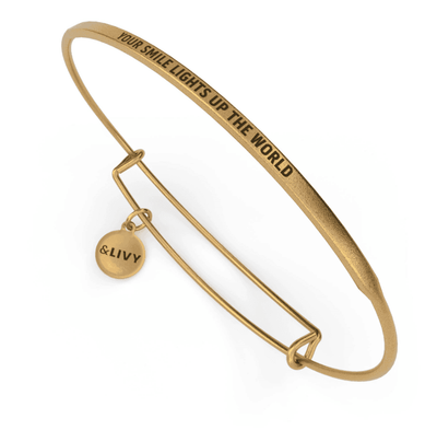 Gold bangle bracelet with "Your smile lights up the world" engraved in cursive.