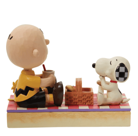 Jim Shore figurine of Charlie Brown, Snoopy, and Woodstock enjoying a picnic on a red quilted blanket, hand-painted in folk art style.