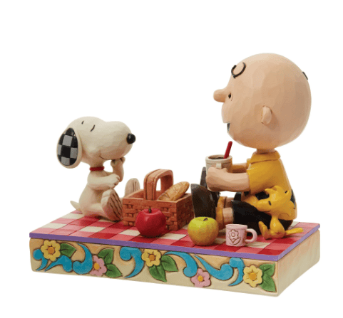 Jim Shore figurine of Charlie Brown, Snoopy, and Woodstock enjoying a picnic on a red quilted blanket, hand-painted in folk art style.
