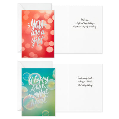 Boxed birthday cards with colorful soft-focus backgrounds, script lettering, silver foil accents, and envelopes, four bright cheerful designs.
