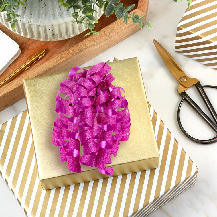 Hallmark pink curly gift bow with glittery corkscrew ribbon strands and self-adhesive backing, perfect for wrapped birthday presents.
