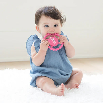 Pink round silicone teether with beaded edges and "Hello Gorgeous" phrase, designed for babies to chew and grip easily.