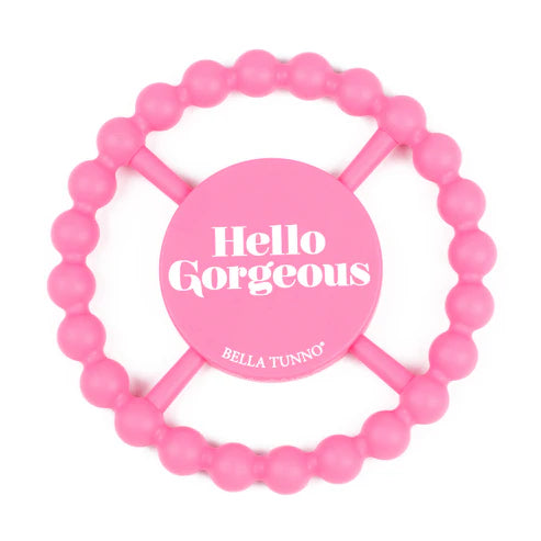 Pink round silicone teether with beaded edges and "Hello Gorgeous" phrase, designed for babies to chew and grip easily.