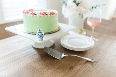 White pinstripe square cake pedestal, 13 inches wide, dishwasher and microwave safe, from Nora Fleming collection.

