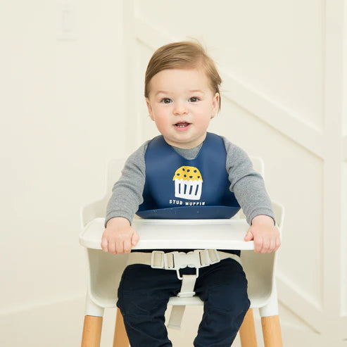 Navy blue silicone baby bib with “Stud Muffin” phrase, featuring a large food-catching pocket and adjustable neck closure.

