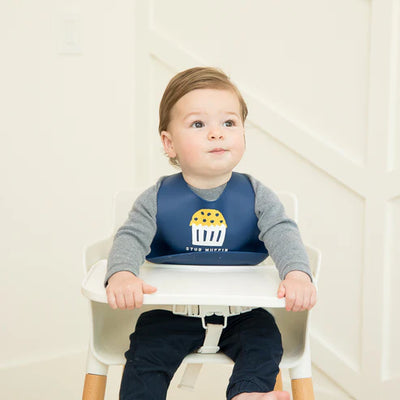 Navy blue silicone baby bib with “Stud Muffin” phrase, featuring a large food-catching pocket and adjustable neck closure.


