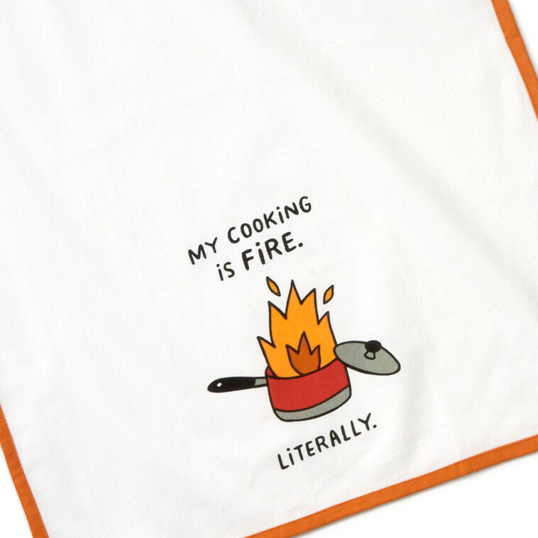 White cotton tea towel with orange border, featuring a flaming pot illustration and the message: “My cooking is fire.
