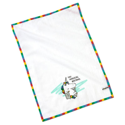 White cotton tea towel with rainbow-striped border and unicorn in chair, featuring the message: “You magical bastard.”