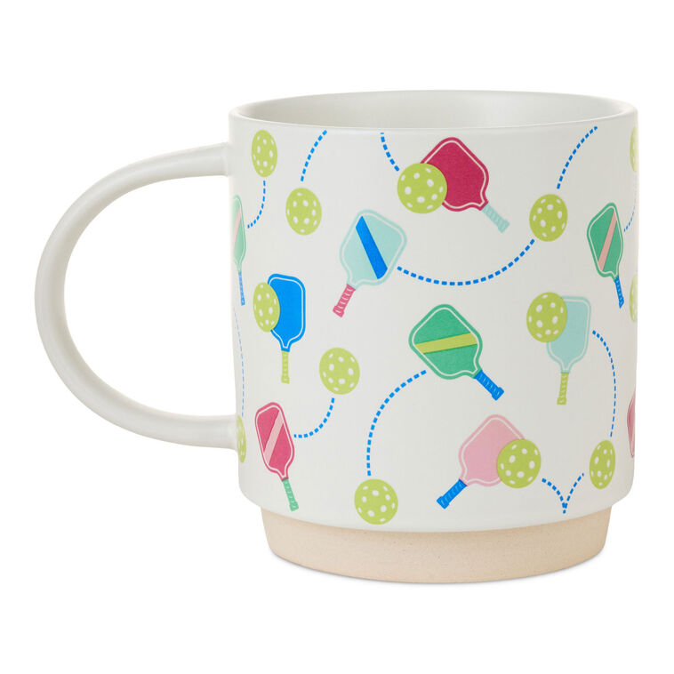 White ceramic pickleball mug with colorful paddle and ball icons, oversized handle, and stackable recessed base