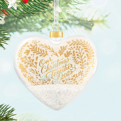 Glass heart Christmas ornament with snow, gold greenery accents, and “Our Christmas Together 2025” message.

