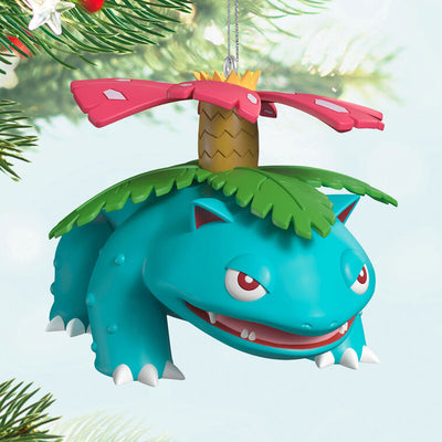 Hallmark Keepsake Pokémon Venusaur ornament with pink blossom on its back, blue-green body, red eyes, and festive Christmas style.