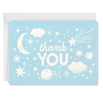 Blue thank-you cards with white embossed designs of a crescent moon, stars, clouds, and planets, shown with matching envelopes in a gift box.
