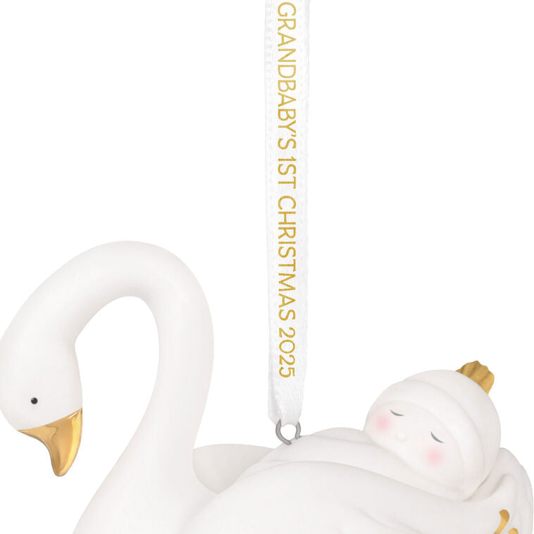 Porcelain Christmas ornament of a baby nestled in a swan’s wings, with gold accents and a commemorative 2025 ribbon

