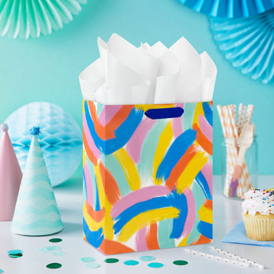 Hallmark medium gift bag with colorful abstract brushstroke rainbows in purple, blue, yellow, and orange on a white background