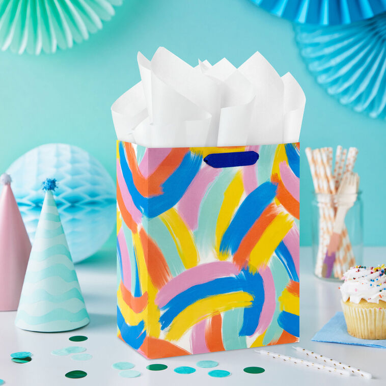 Hallmark medium gift bag with colorful abstract brushstroke rainbows in purple, blue, yellow, and orange on a white background