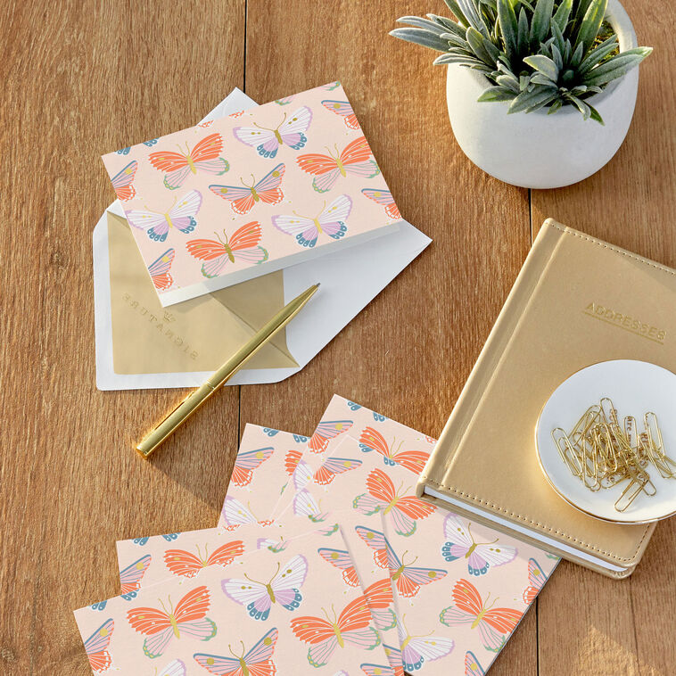 Blank note cards with colorful butterfly illustrations and gold foil accents on a soft peach background.