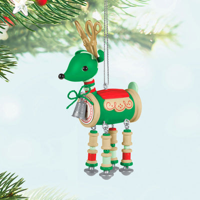 Green reindeer ornament made of red and green thread spools with gold scissors antlers, button tail, and silver thimble bell

