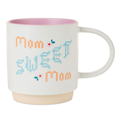 White ceramic mug with “Mom Sweet Mom” in colorful cross-stitch-style lettering and floral accents, oversized handle.