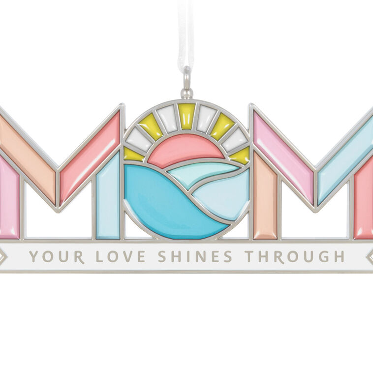 Stained-glass style metal ornament spelling “Mom” with sun and waves in the O, and banner reading “Your love shines through.”