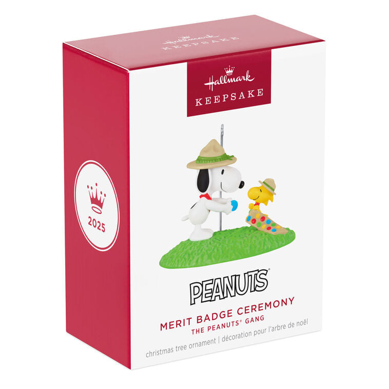 Snoopy in scout hat presenting merit badge to Woodstock in sash, standing on green grass, Hallmark Peanuts Christmas ornament collectible
