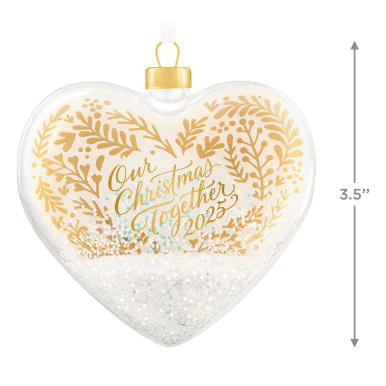 Glass heart Christmas ornament with snow, gold greenery accents, and “Our Christmas Together 2025” message.

