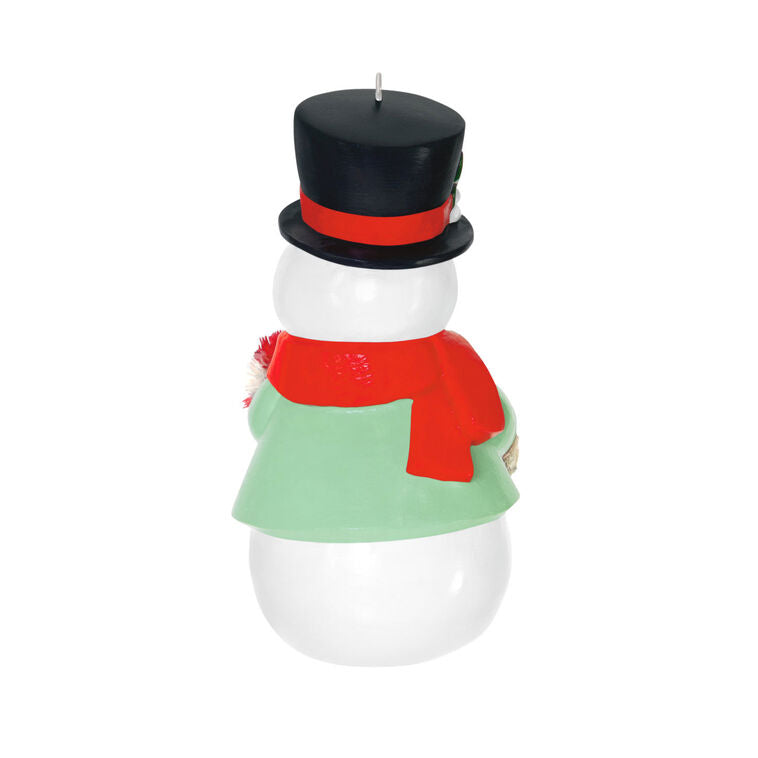 Porcelain snowman ornament in festive coat, scarf, and top hat holding a bottlebrush candy cane